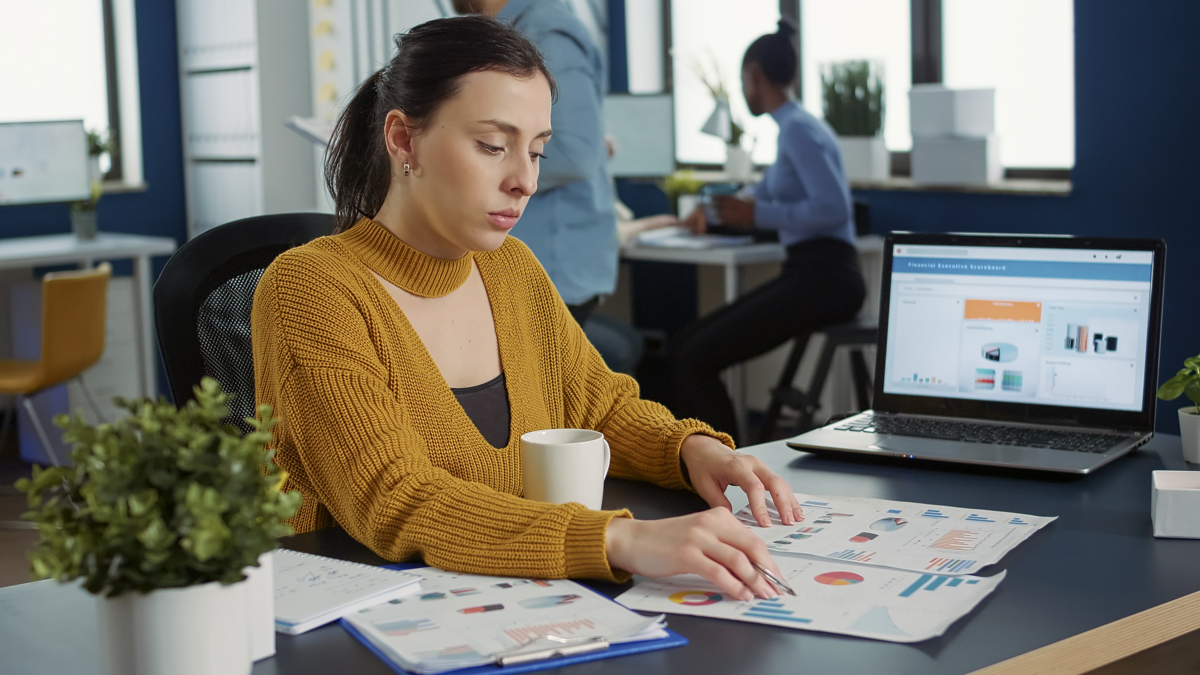 portrait-startup-employee-comparing-two-sheets-paper-with-charts-analyzing-financial-data-while-drinking-morning-coffee-woman-working-busy-marketing-department-sitting-desk-with-laptop-min